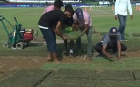 Ground staff at the Greater Noida cricket ground replace sodden sections of the outfield.