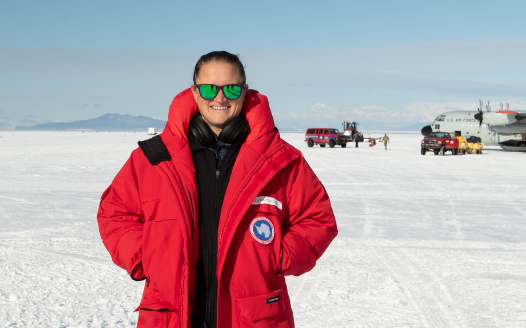 A waist-up portrait of Molly Patterson in Antarctica, wearing a bright red jacket and sunglasses, with a snowy plain behind her.