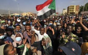 Sudanese protesters lift national flags as they rally on 60th Street in the capital Khartoum, to denounce overnight detentions by the army of government members.