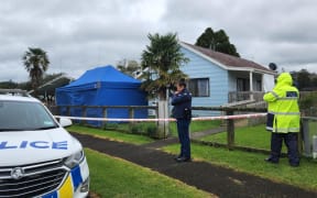Police are executing a search warrant at a house on Taraire Street in relation to the investigation into the homicide of Linda Woods. At least four officers are guarding the cordoned house and other officers can be seen rummaging through rubbish bins on the property.