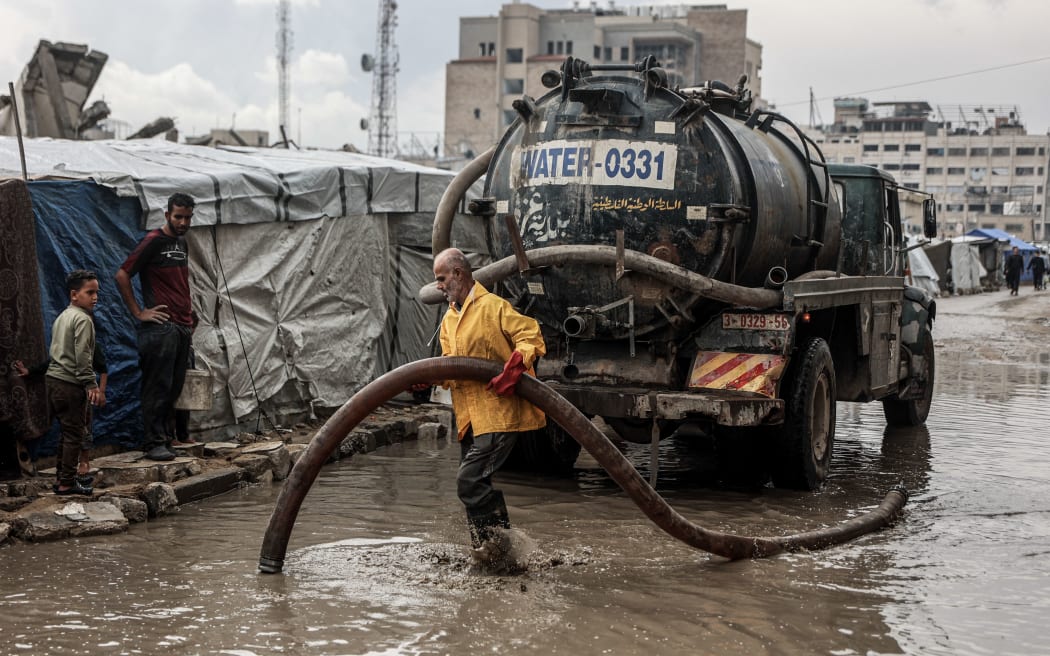 A Palestinian man clears stagnant water from the road near a displacement camp after the first winter rainfall in Gaza City on Friday.