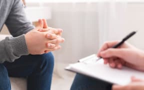 Therapist writing notes during counseling session with single man sitting on couch, panorama, empty space