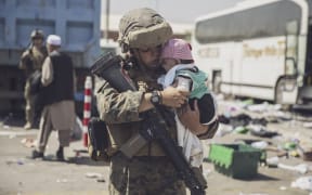 This US Marine photo released August 29, 2021 shows a US Marine with the 24th Marine Expeditionary Unit (MEU) carrying a baby as the family processes through the Evacuation Control Center (ECC) during an evacuation at Hamid Karzai International Airport, Kabul, Afghanistan, on August 28, 2021.