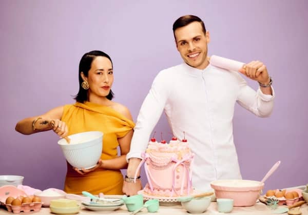 Melissa Leong stirs something in a bowl while Amaury Guichon slings a rolling pin over his shoulder.