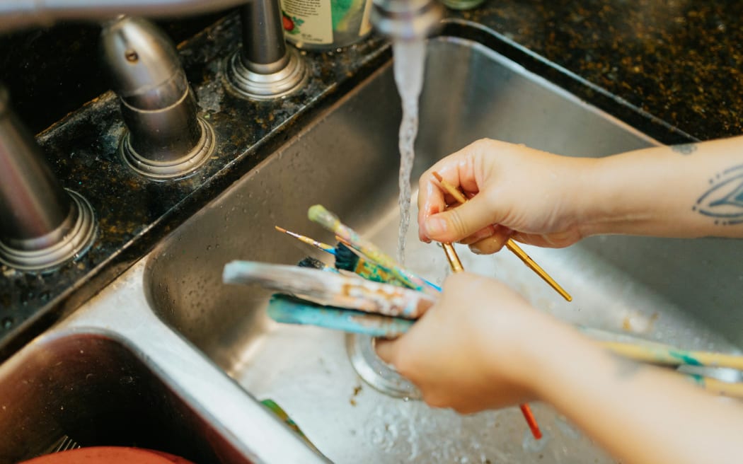 Paintbrushes being cleaned in a sink under running water of tap.