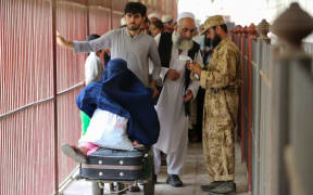 Afghans cross into Pakistan while a security personnel stands guard at the Pakistan-Afghanistan border in Torkham on September 15, 2023. The Torkham border crossing between Afghanistan and Pakistan reopened to pedestrians and vehicles early on September 15, a senior official told AFP, more than a week after it was closed following a gun battle between frontier guards. Islamabad and Kabul have been in diplomatic deadlock since September 6, when border guards opened fire at the crossing -- halfway between the two capitals -- in a dispute over an Afghan outpost being constructed. (Photo by Shafiullah KAKAR / AFP)