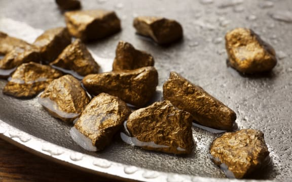 Plate with gold nuggets and water on table, closeup.