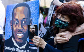 Racial justice demonstrations were held around the US after word of Ahmaud Arbery's death spread. A woman holds a portrait of Arbery, and George Floyd at a remembrance event in May 2021 in Minneapolis..