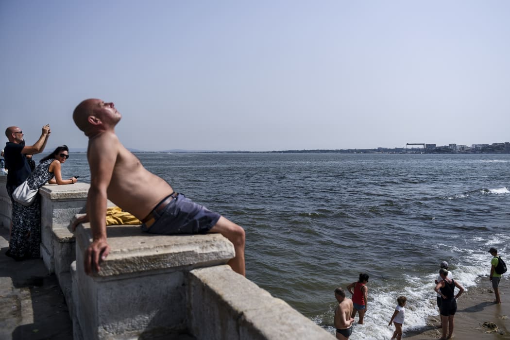 A man sunbathes as others cool off in Tagus River at Ribeira das Naus in Lisbon.