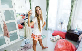 10 years old pre teen girl choosing outfit in her closet. Messy in the bedroom, clotning on the floor. Teenager is dressing up and taking selfie in the morning.