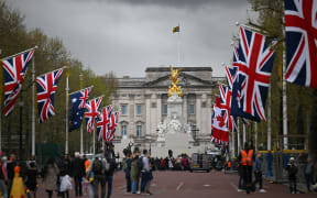 People walk beneath flags of the Union and Commonwealth on The Mall, looking towards Buckingham Palace, in central London, on April 28, 2023 ahead of the coronation ceremony of Charles III and his wife, Camilla, as King and Queen of the United Kingdom and Commonwealth Realm nations, on May 6, 2023. (Photo by Daniel LEAL / AFP)
