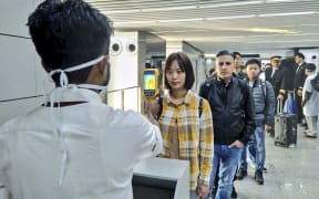 In this handout photograph taken and released by the Ministry of Civil Aviation (MoCA) on January 21, 2020, a man (L) uses a thermographic camera to screen the head of people at Netaji Subhash Chandra Bose International Airport in Kolkata.