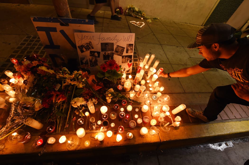 A student lights a candle at a makeshift memorial outside the IV Deli Mart where one of the victims of a killing spree was shot and killed .