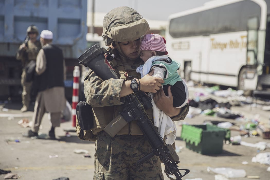 This US Marine photo released August 29, 2021 shows a US Marine with the 24th Marine Expeditionary Unit (MEU) carrying a baby as the family processes through the Evacuation Control Center (ECC) during an evacuation at Hamid Karzai International Airport, Kabul, Afghanistan, on August 28, 2021.