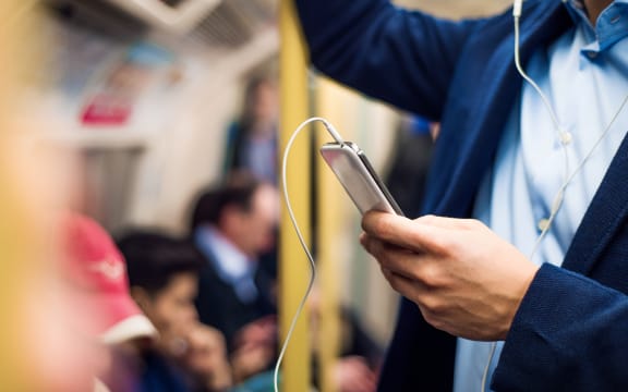 A man wearing headphones uses his smartphone on a train.