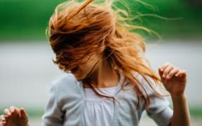 A girl's hair is blown across her face by wind.