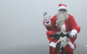 Santa Claus cycles along a street engulfed in fog on Christmas Day 2023 in New Delhi, India.