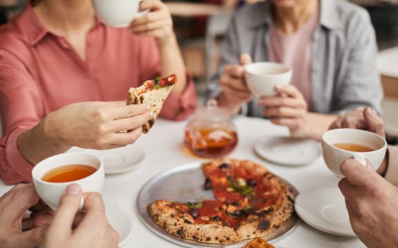 Close-up of woman holding piece of pizza and having lunch together with her family at the table