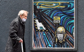 An elderly pedestrian wearing a face mask or covering due to the COVID-19 pandemic, walks past graffiti depicting the subjects within famous artworks, but wearing masks, in Glasgow.