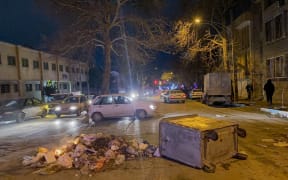 Burning debris lies next to an overturned dumpster in the middle of a street during unrest amid demonstrations in Hamedan, Iran, on January 1, 2026. The demonstrations erupted after shopkeepers in Tehran’s Grand Bazaar shut their businesses to protest the sharp fall of Iran’s currency and worsening economic conditions, with clashes reported in several provinces and Iranian media and rights groups saying multiple people were killed in the violence, marking the largest protests to hit the Islamic Republic in three years. (Photo by Mobina / Middle East Images via AFP)