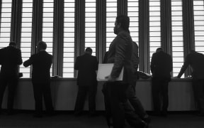 Black and white image of men in suits standing in front of tall window