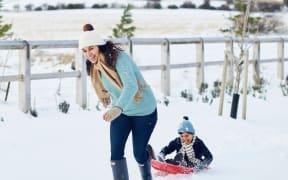 Nadia Lim laughs as she drags her son on a sled through the snow.
