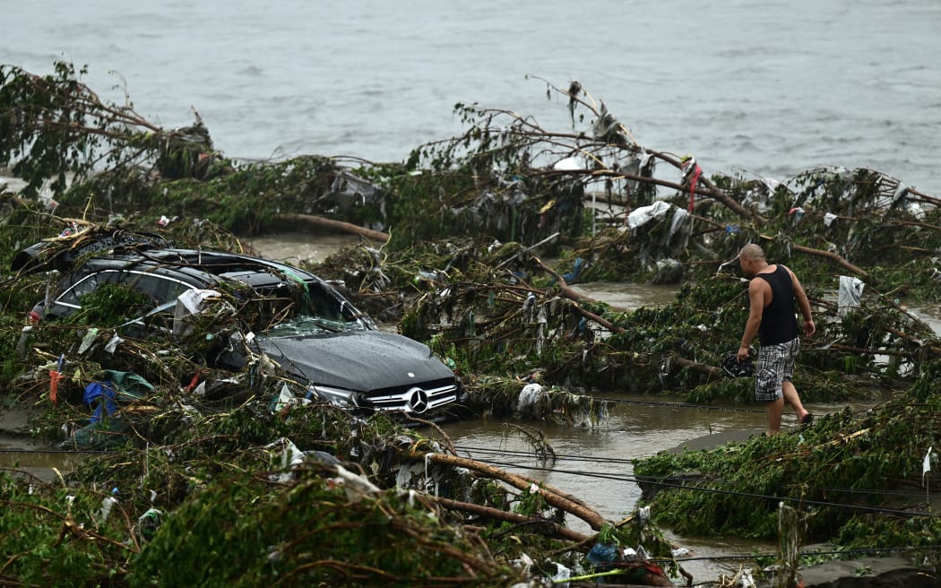 A man looks at a damaged car following heavy rains in Fangshan district in Beijing on August 1, 2023. At least 11 people were killed and 13 were missing after heavy rains lashed Beijing, state media said on August 1, in downpours that have submerged roads and deluged neighbourhoods with mud. (Photo by Pedro PARDO / AFP)