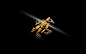 A wooden puppet suspended in darkness with hands holding all its limbs up to a beam of light.