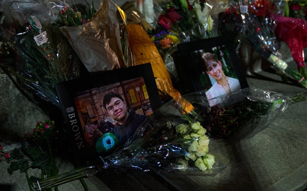 Framed photos of mass shooting victims Mukhammad Aziz Amurzokov and Ella Cook are seen at a makeshift memorial near Brown University in Providence, Rhode Island, on December 15, 2025. A gunman remained at large after a weekend mass shooting at elite Brown University left two dead and nine wounded, with US authorities releasing new footage of a masked "person of interest" captured on surveillance cameras. The shooting took place December 13 in a building where exams were underway on the Ivy League campus in Providence, Rhode Island when a man with a rifle burst in and opened fire before fleeing. (Photo by Bing Guan / AFP)