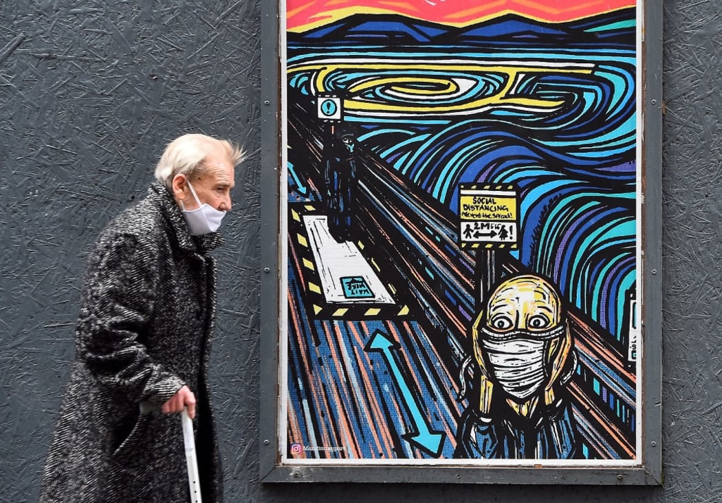 An elderly pedestrian wearing a face mask or covering due to the COVID-19 pandemic, walks past graffiti depicting the subjects within famous artworks, but wearing masks, in Glasgow.