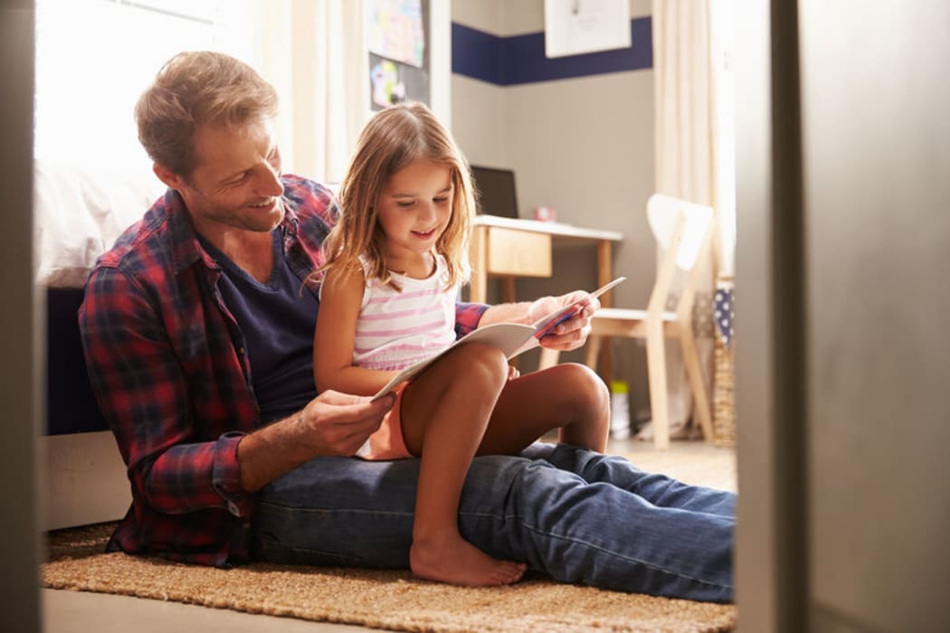 A photo of a father and young daughter reading together