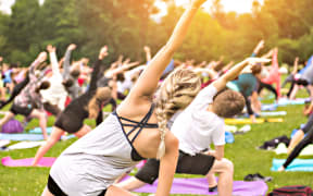 A big group of adults attending a yoga class outside in park