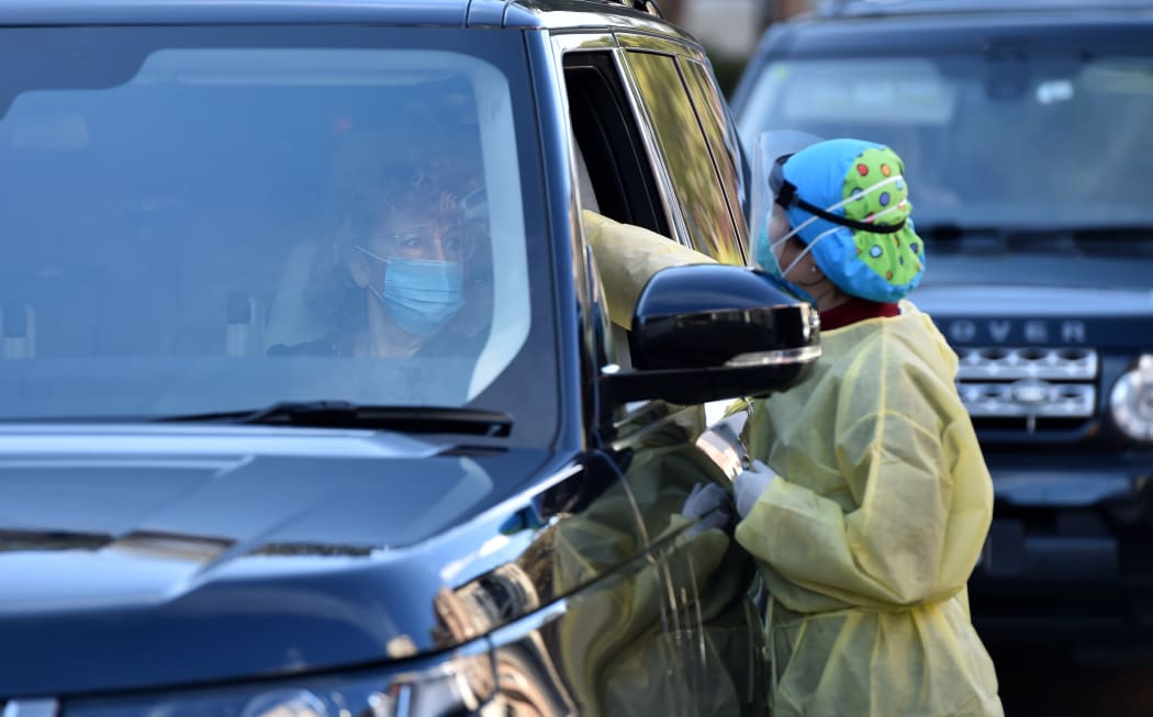 A medic (R) takes a woman's temperature at a drive-through testing centre for the COVID-19 coronavirus in Sydney on July 30, 2020. (Photo by PETER PARKS / AFP)