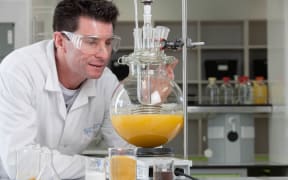 Warren Grigsby in a chemistry lab with a large vial of bio-based resin