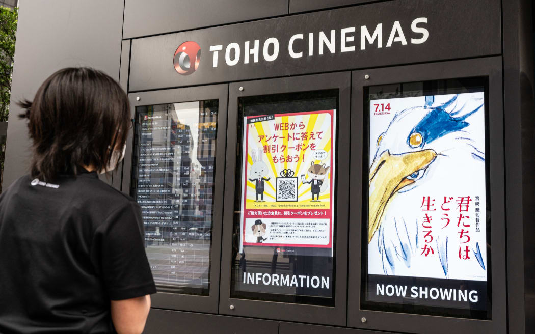 A cinema employee checks on a display showing a digital poster (R) for Oscar-winning animator Hayao Miyazaki's latest film, titled in English "How Do You Live?", on the first day of its premiere in Tokyo on July 14, 2023. Miyazaki's much-anticipated film -- his first feature in a decade and probably his last -- was released in theatres in Japan on July 14.