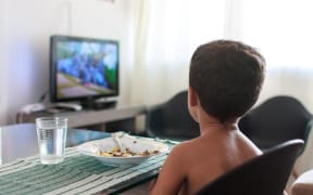 A young boy distracted watching TV while eating lunch