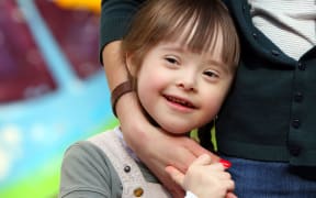 Close up of girl beign cuddled against her mother's hip