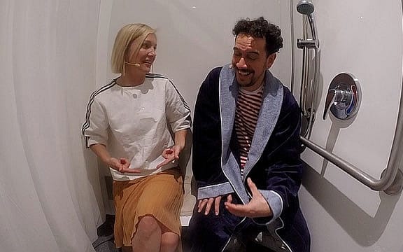 Hayley Holt and James Nokise sitting side by side in a shower and laughing.