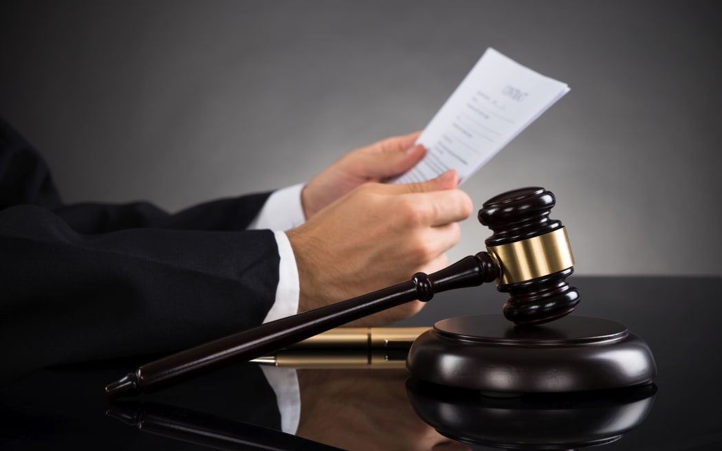 Close-up Of Judge Holding Document With Gavel At Desk