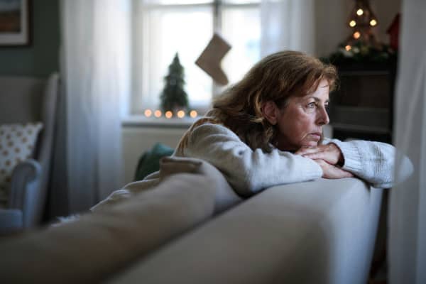 An older woman looks out the window while sitting on a sofa.