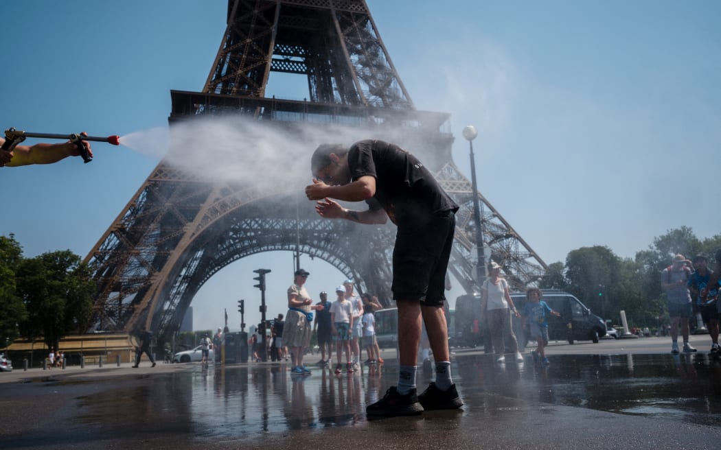 A municipal employee sprays water to cool off tourists in front of the Eiffel Tower in Paris, on July 2, 2025, as a heatwave hits France. France registered its second-warmest June since records began in 1900, said the country's ministry for ecological transition on July 2, 2025, as Europe swelters under an early summer heatwave. (Photo by Dimitar DILKOFF / AFP)
