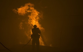A firefighter hoses down burning pipes near a water tank at the Sand Fire near Santa Clarita, California.