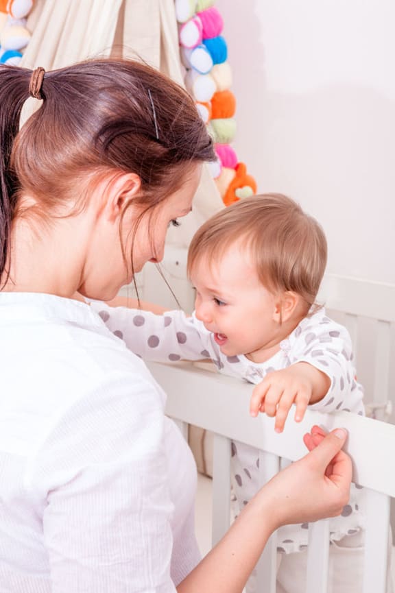 A photo of a baby who is having bad dreams with her mother standing at the cot.