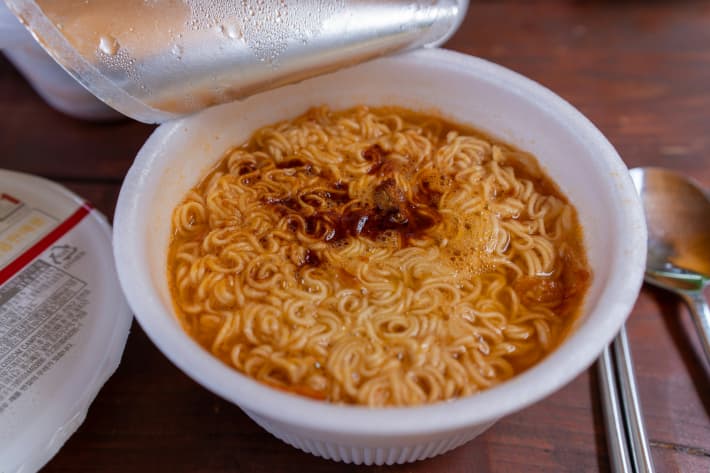 An opened plastic container of cooked instant noodles.