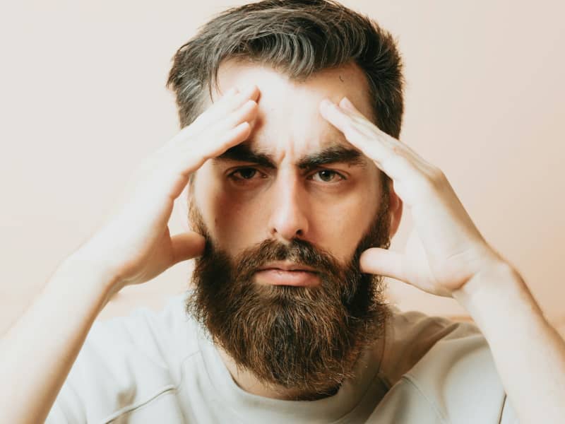 A bearded white man holds his hands to his head.