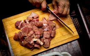 A person chops raw meat on a wooden chopping board.