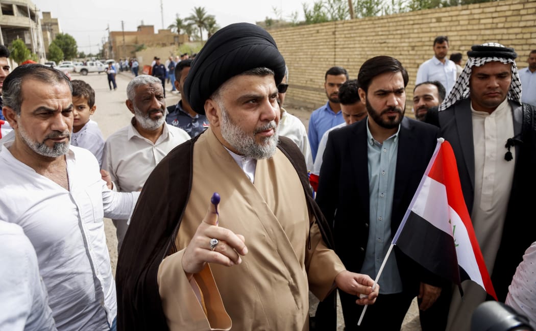 Iraqi Shiite cleric and leader Moqtada al-Sadr (C-L) shows his ink-stained index finger and holds a national flag while surrounded by people outside a polling station in the central holy city of Najaf on May 12, 2018