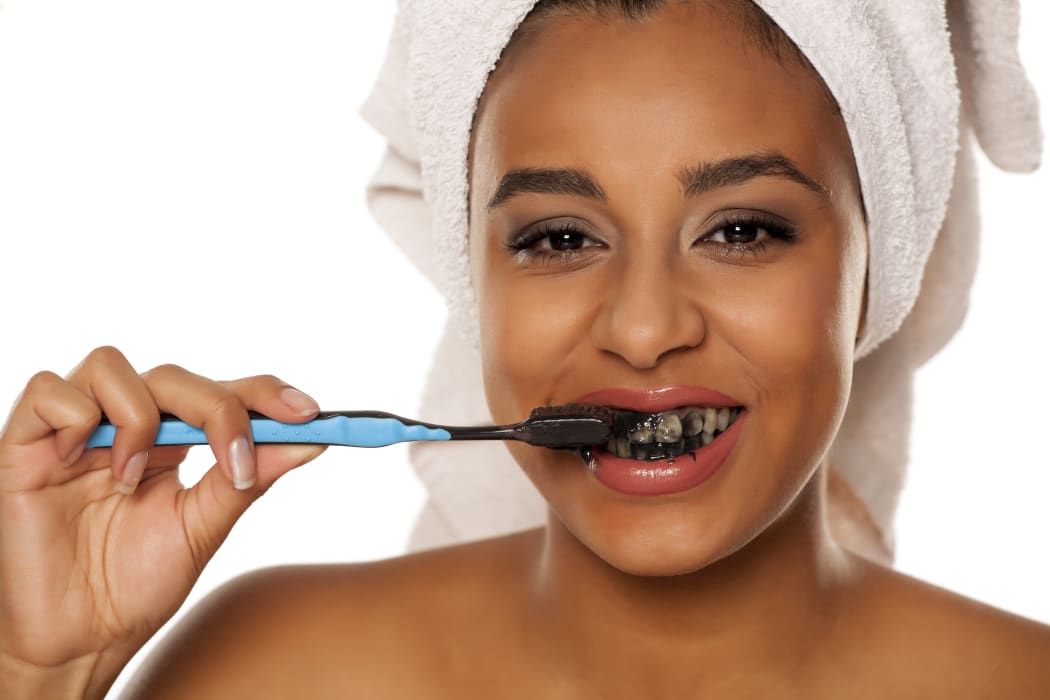 portrait of a happy young woman brushing her teeth with black toothpaste on a white background