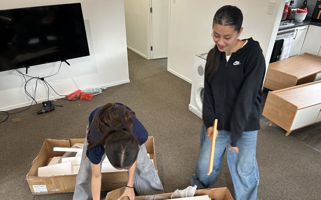 Picture of two young women smiling at camera, sitting among furniture pieces.