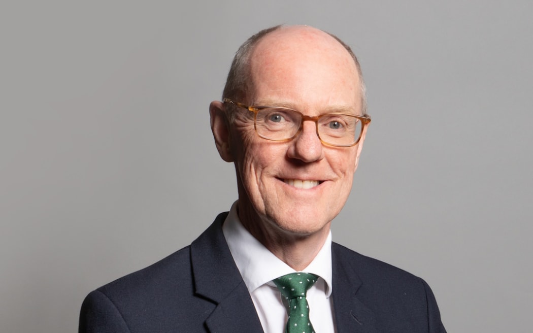 Nick smiles at the camera. he wears a suit and a green spotted tie.